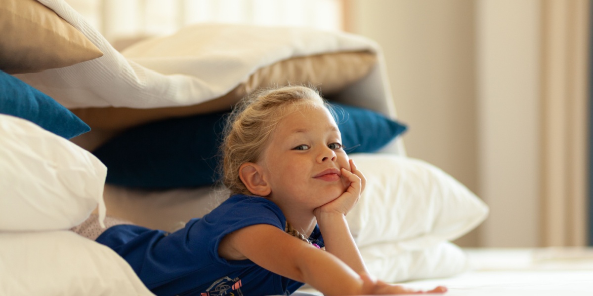 Young child lying on a stack of pillows, pretending to relax in a cozy indoor bird nest made from blankets and cushions.