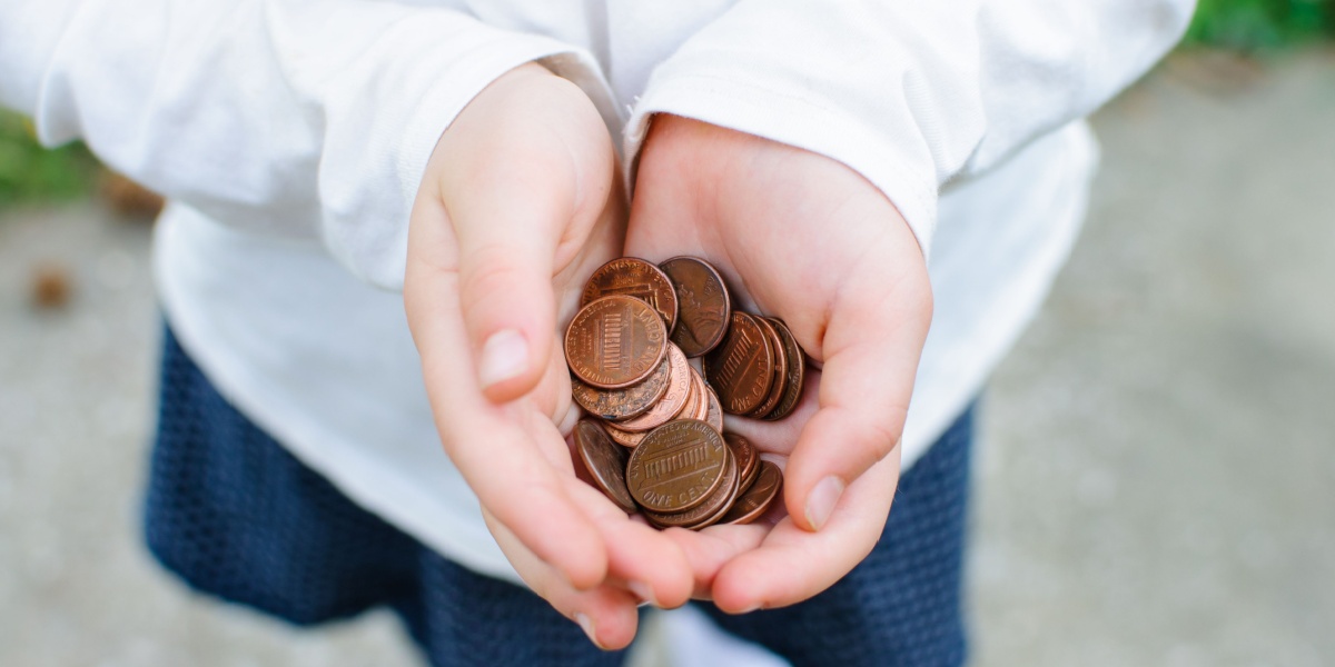 An image of a child standing outside with their hands holding a pile of pennies.