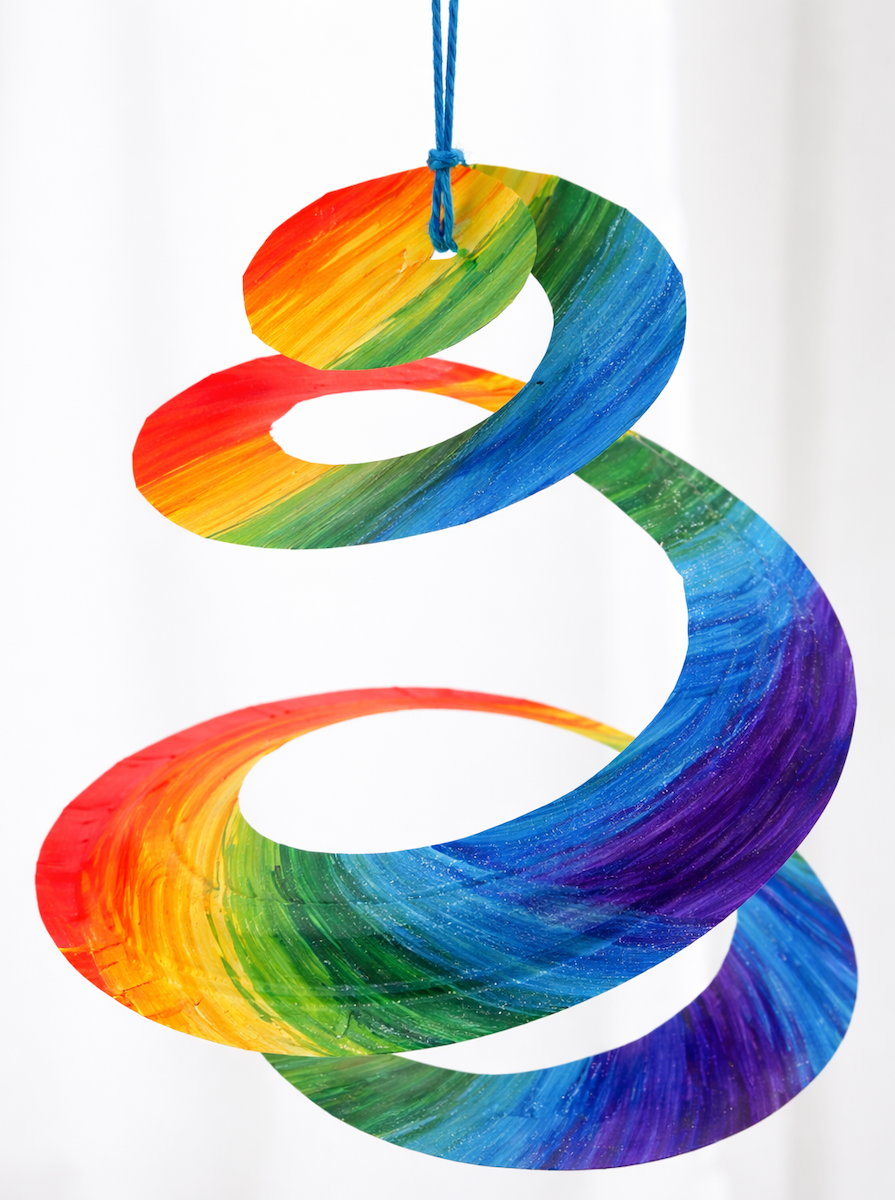A hanging spiral craft painted in bright rainbow colors, suspended by a blue string and twisting downward in a colorful swirl.