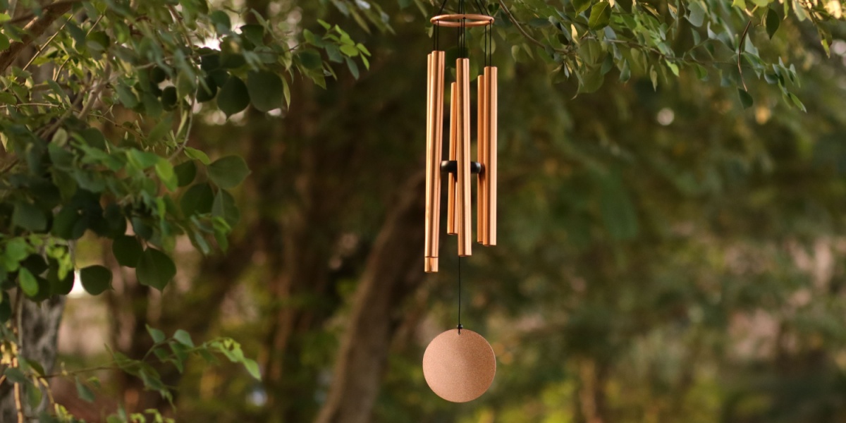 Wooden wind chimes hanging from a tree branch outdoors on a breezy spring day.