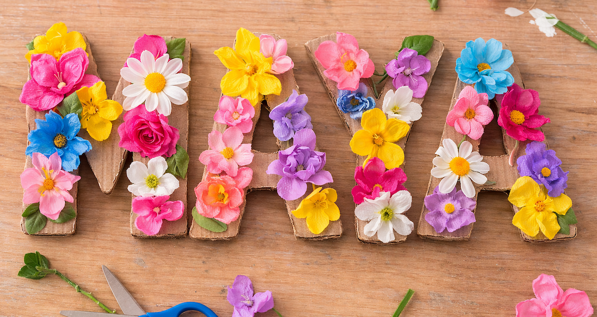 Letters spelling “SPRING” decorated with colorful artificial flowers on a wooden surface.