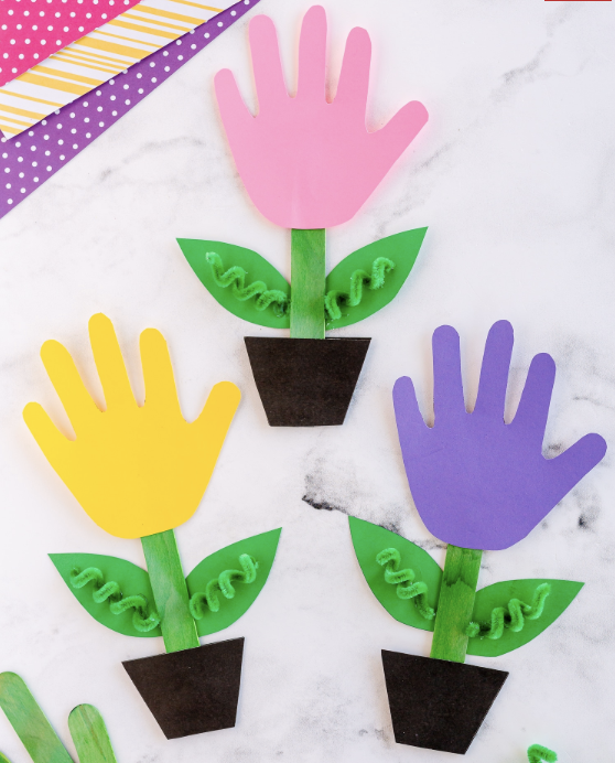 Colorful handprint flowers in pots made from paper cutouts on a white background.