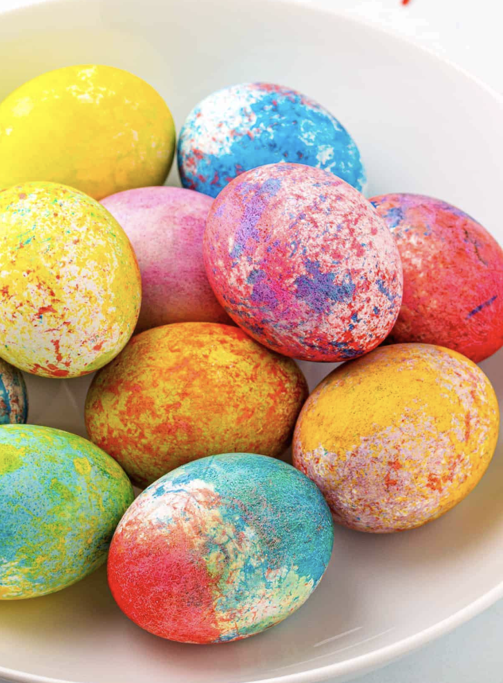 Close-up of brightly colored Easter eggs with speckled and splattered paint effects in yellow, pink, blue, orange, and green.