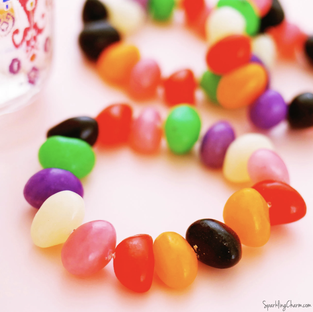 Colorful jelly beans strung together to form a bracelet, arranged in a circle on a white surface.