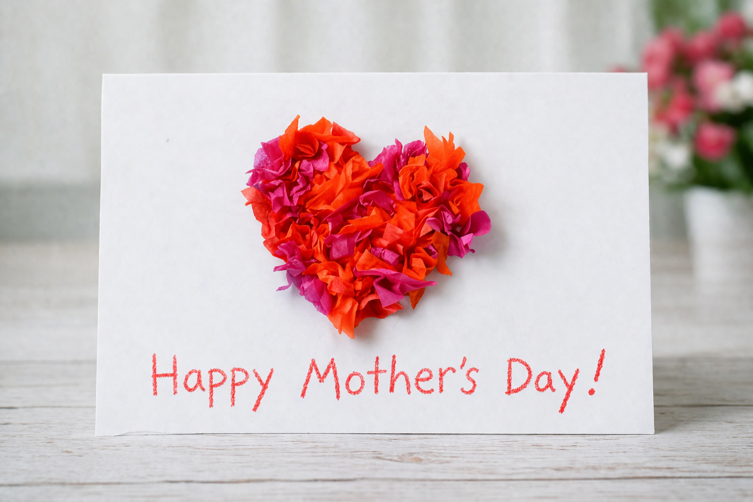 White handmade Mother’s Day card featuring a heart made from crumpled red and pink tissue paper, with the message “Happy Mother’s Day!” written below.