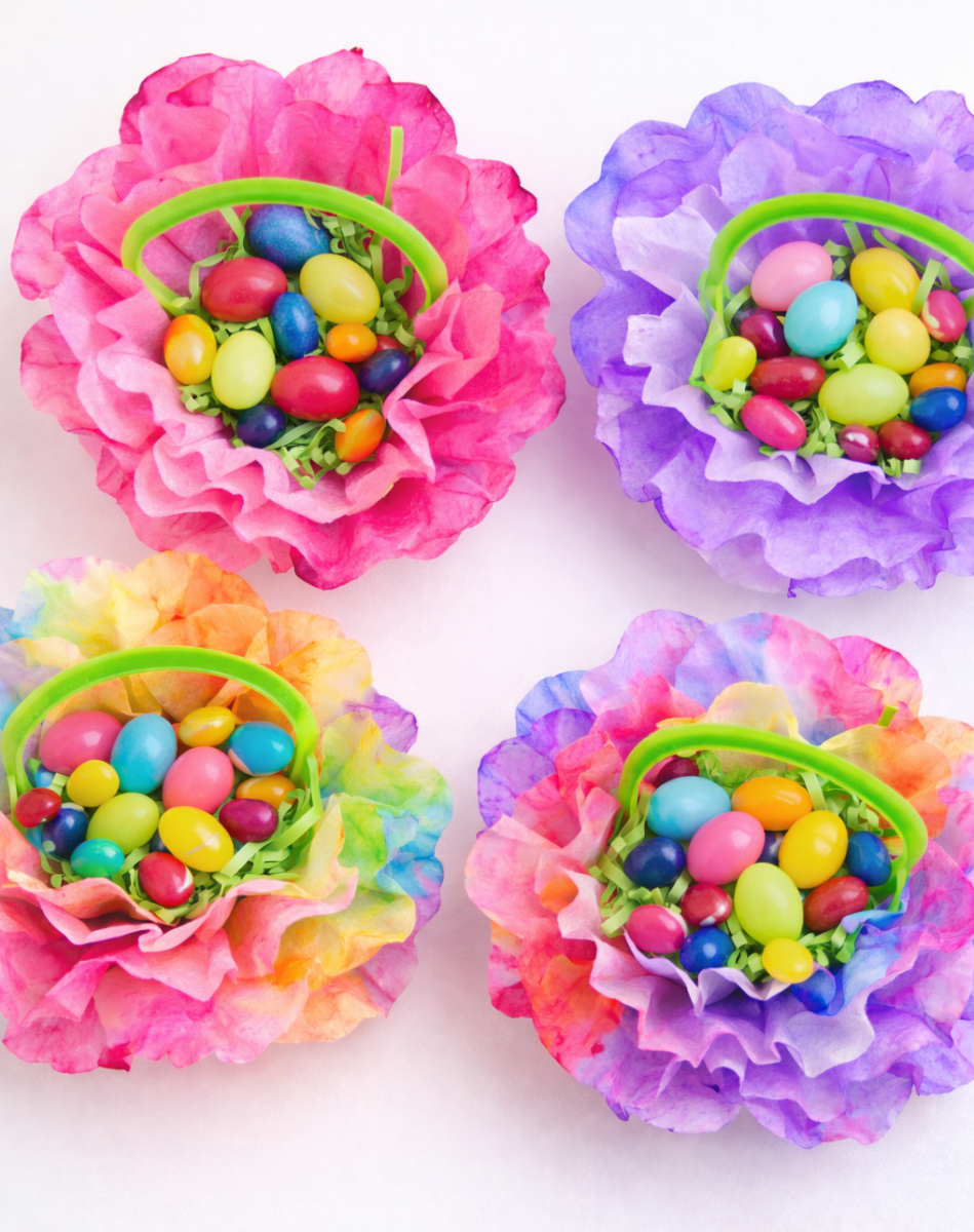 Colorful tissue paper flower baskets filled with assorted jelly beans and candy eggs, each with a small green handle.