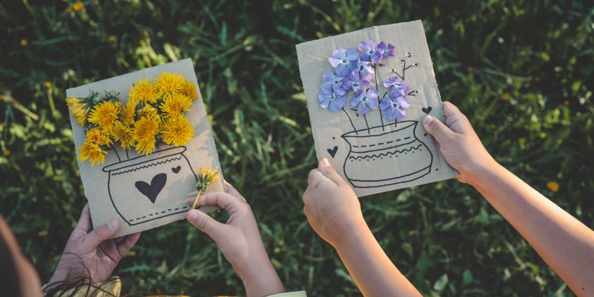 Children holding handmade cards decorated with real pressed flowers arranged in drawn vases.