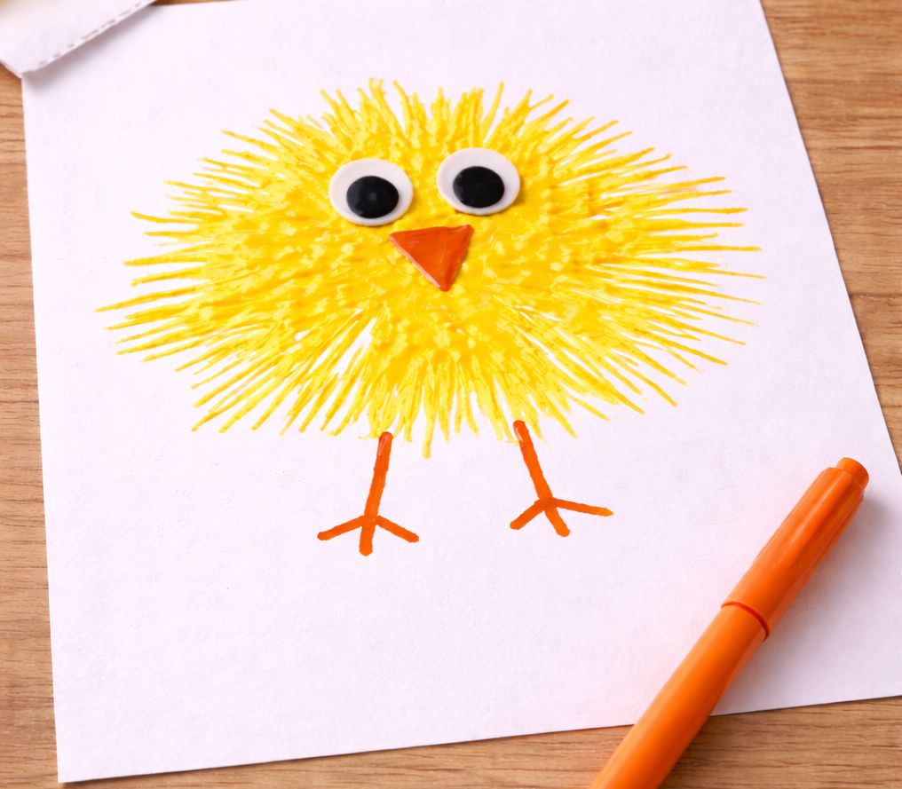 Yellow chick drawing made with radiating marker strokes, featuring googly eyes, an orange triangle beak, and simple orange stick legs on white paper.