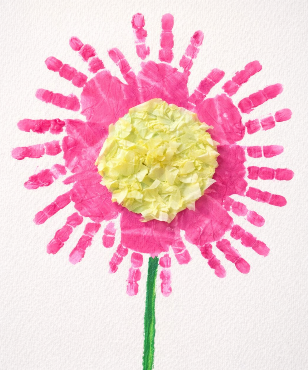 Pink handprint flower with a textured yellow center on white paper.