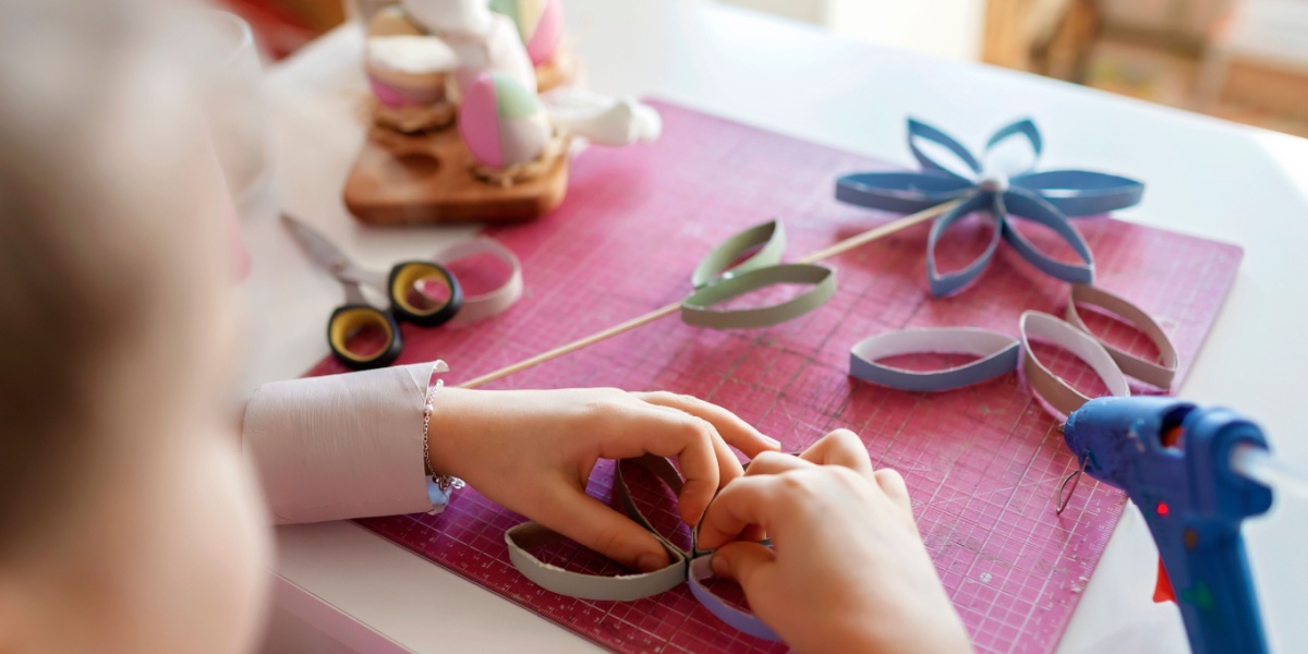 Child assembling a flower using colorful paper loops on a craft mat with scissors and supplies nearby.