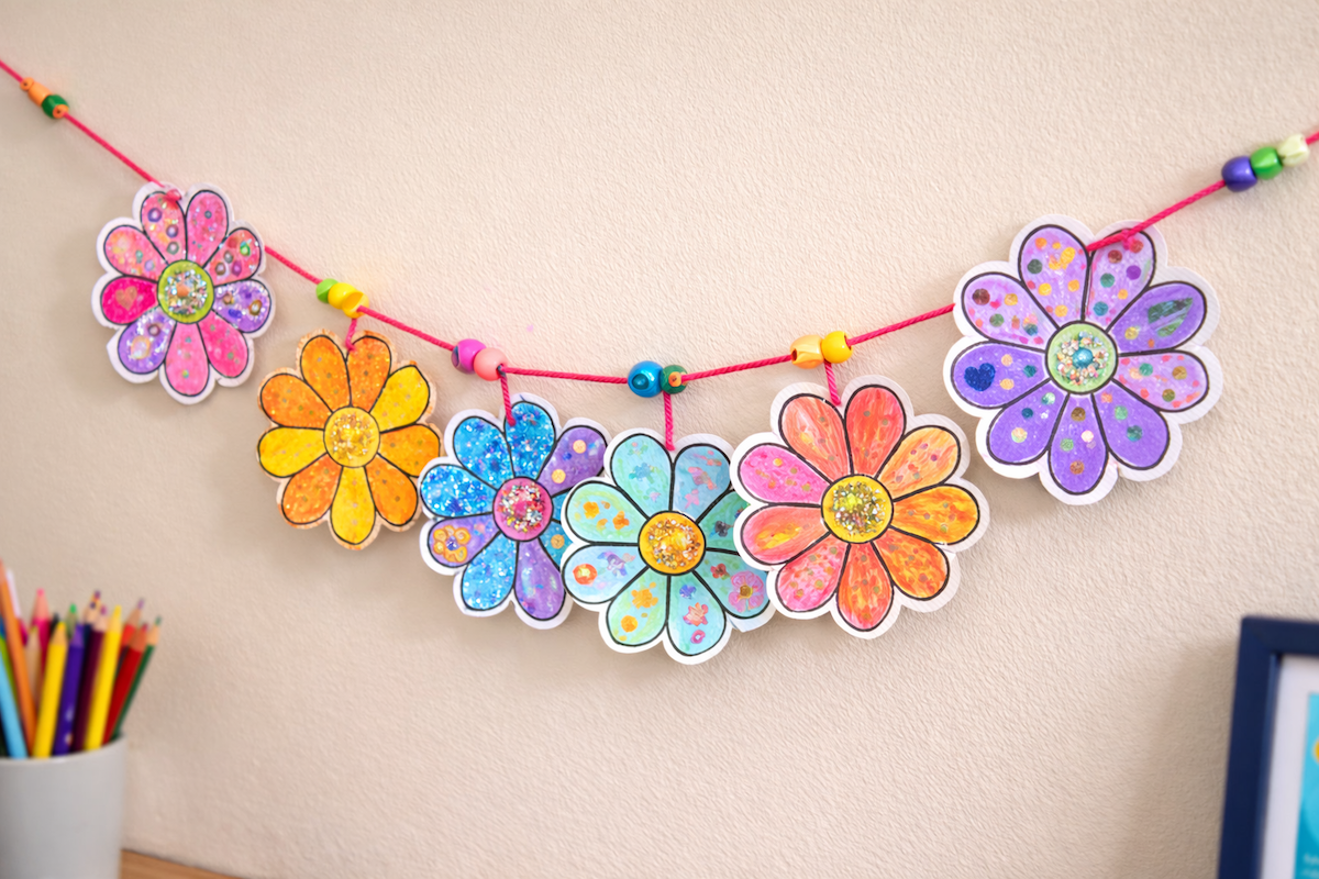 Colorful hand-decorated paper flowers strung together as a hanging garland on a wall.