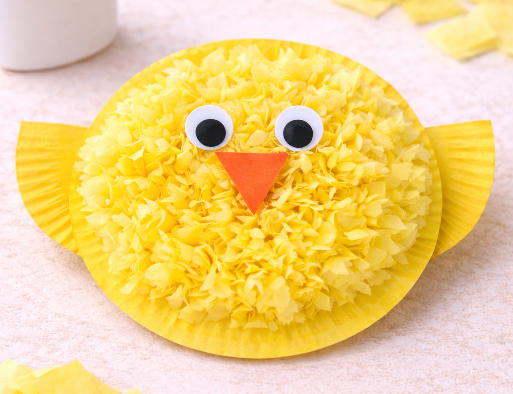 Yellow paper plate chick craft covered in crumpled tissue paper, with large googly eyes and an orange triangle beak.