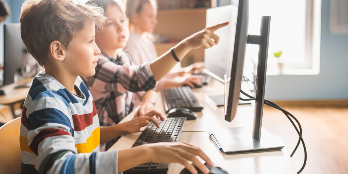 Students seated at desks and working on laptop computers. one student is pointing at their classmate's computer screen.