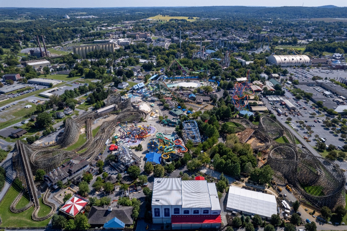 Aerial view of a large amusement park with multiple roller coasters, water slides, and surrounding trees and buildings.