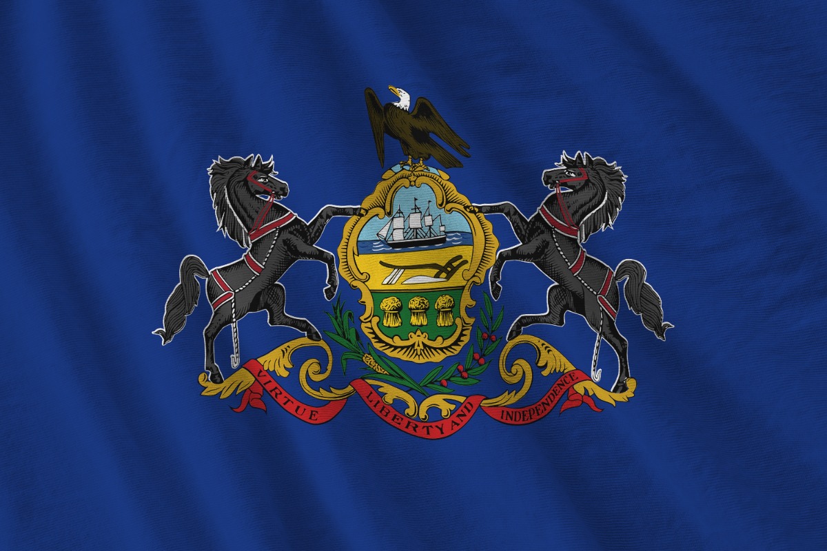 Blue Pennsylvania state flag featuring the coat of arms: two black horses supporting a shield with an eagle on top and a motto ribbon reading 'Virtue Liberty and Independence'