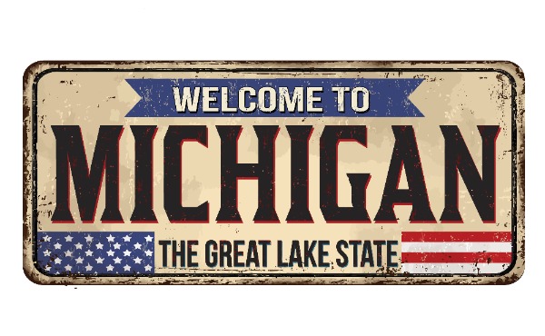 Vintage distressed sign reading 'Welcome to Michigan, The Great Lake State' with a small American flag motif on the bottom left and right edges.