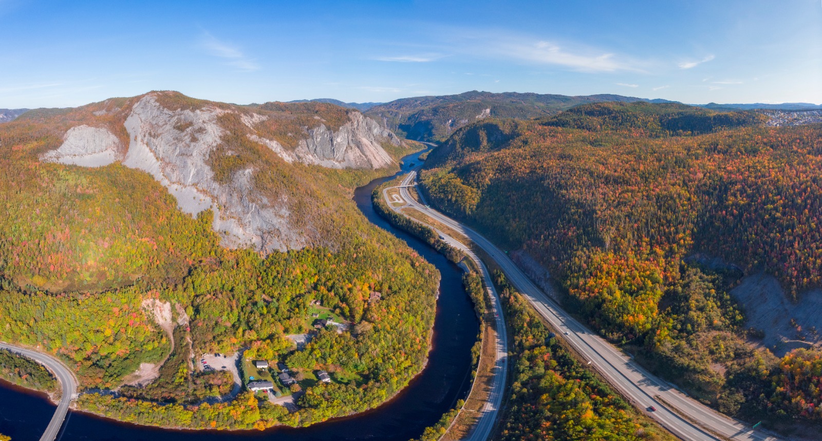 Aerial view of a winding river and section of highway through a colorful autumn forest valley.