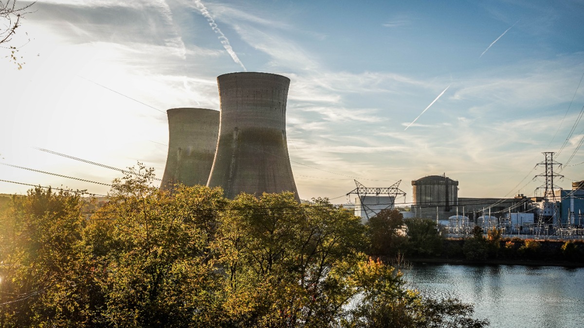 Nuclear power plant with two large cooling towers behind trees by a river at sunset/sunlight glow on the left side.