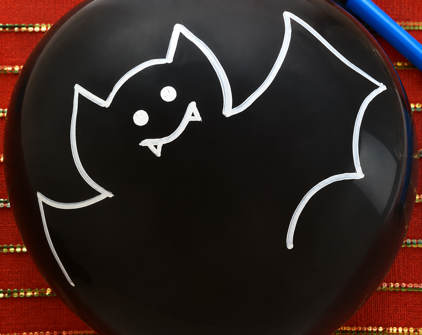 Simple white chalk drawing of a smiling Halloween bat on a black surface.