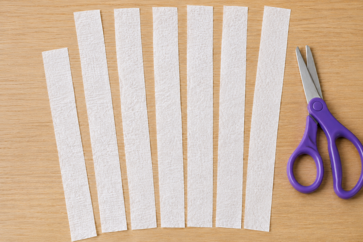 White crepe paper cut into long strips for a ghost windsock craft, with child-safe scissors beside them.