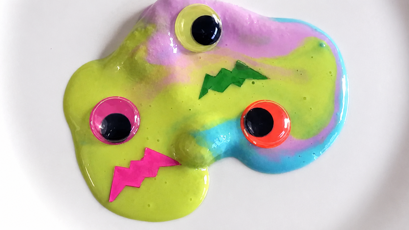 Colorful Halloween monster slime decorated with googly eyes and bright paper facial features.