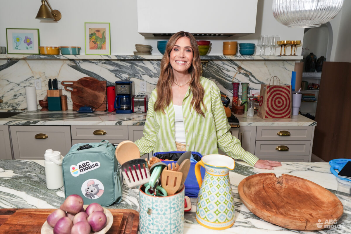 Mandy Moore standing in a kitchen behind a counter with ABCmouse-branded materials and colorful kitchen accessories.