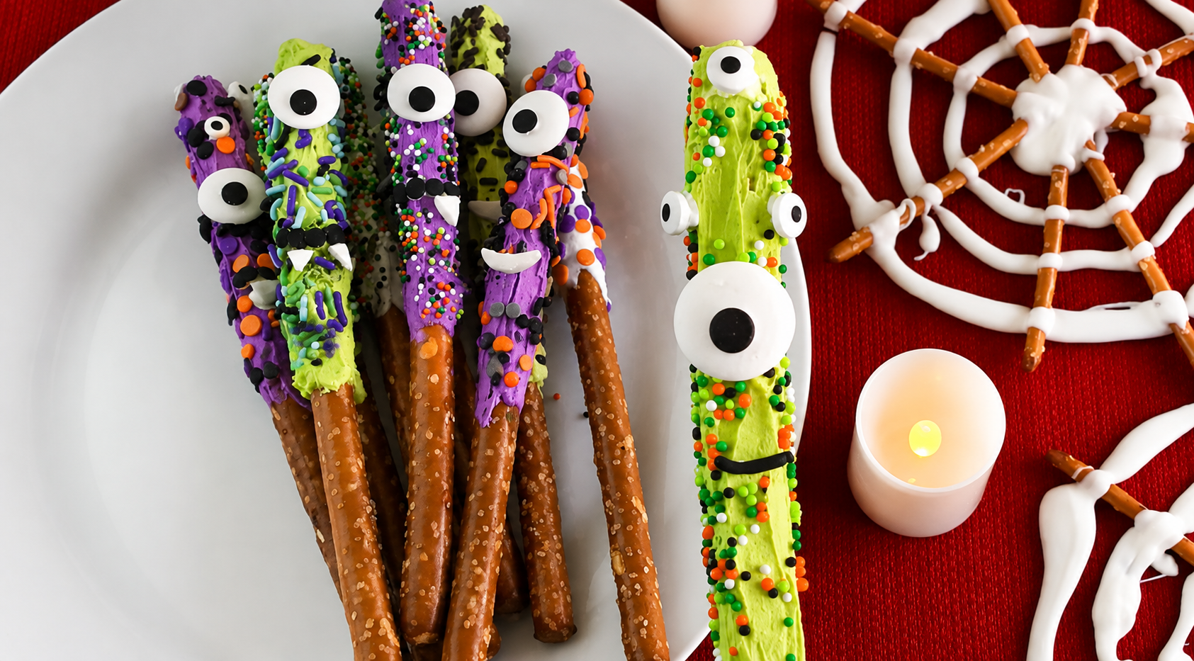 Chocolate-covered pretzel rods decorated as colorful Halloween monsters with candy eyes and sprinkles.