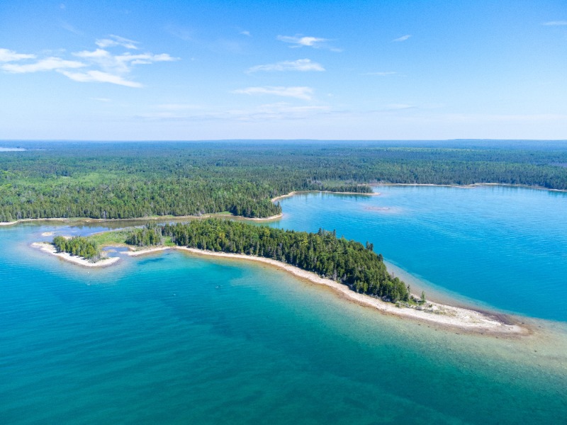 Aerial view of a forested peninsula extending into turquoise sea with sandy shores along the coastline.