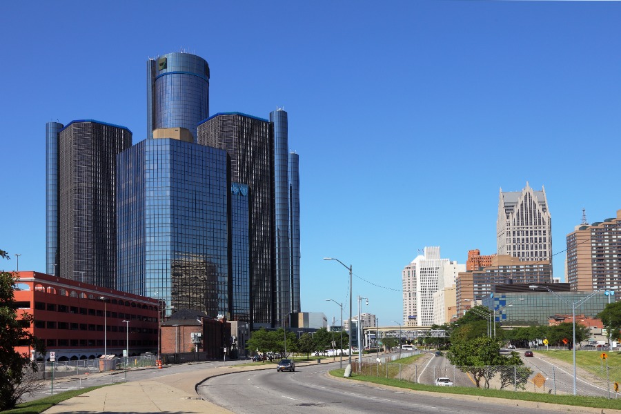City skyline with tall glass skyscrapers along a curved street in daylight, blue sky above.