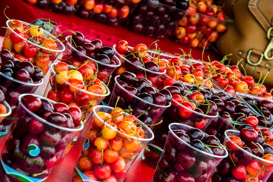Plastic cups filled with red and yellow cherries for sale at a market stall, bright colorful display
