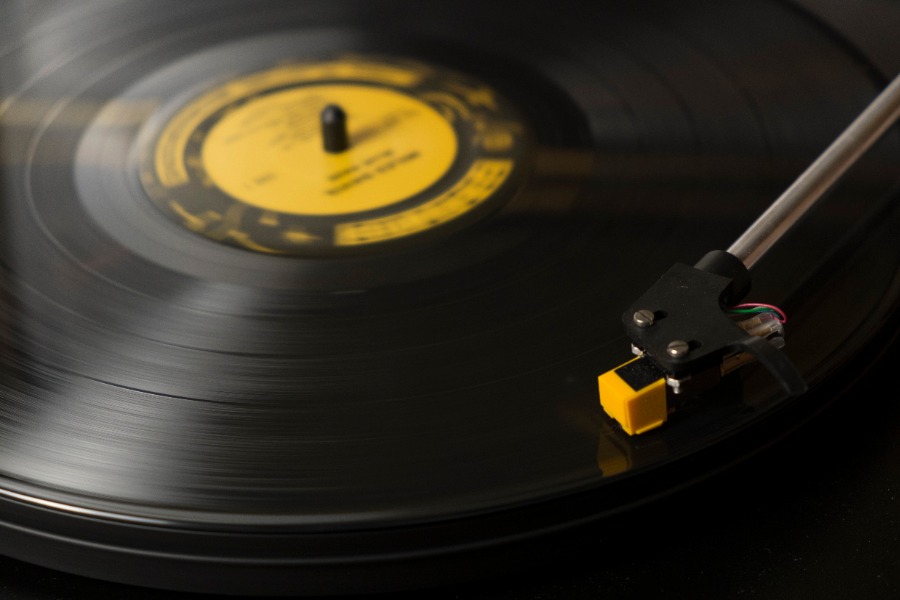 Close-up of a vinyl record spinning on a turntable with the stylus resting in the groove near the orange/yellow label center.