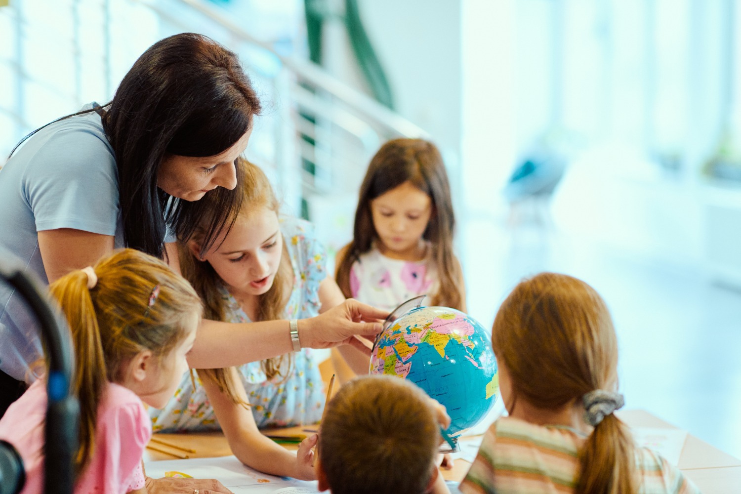 Teacher guides several children as they study a globe during a geography lesson in a bright classroom.