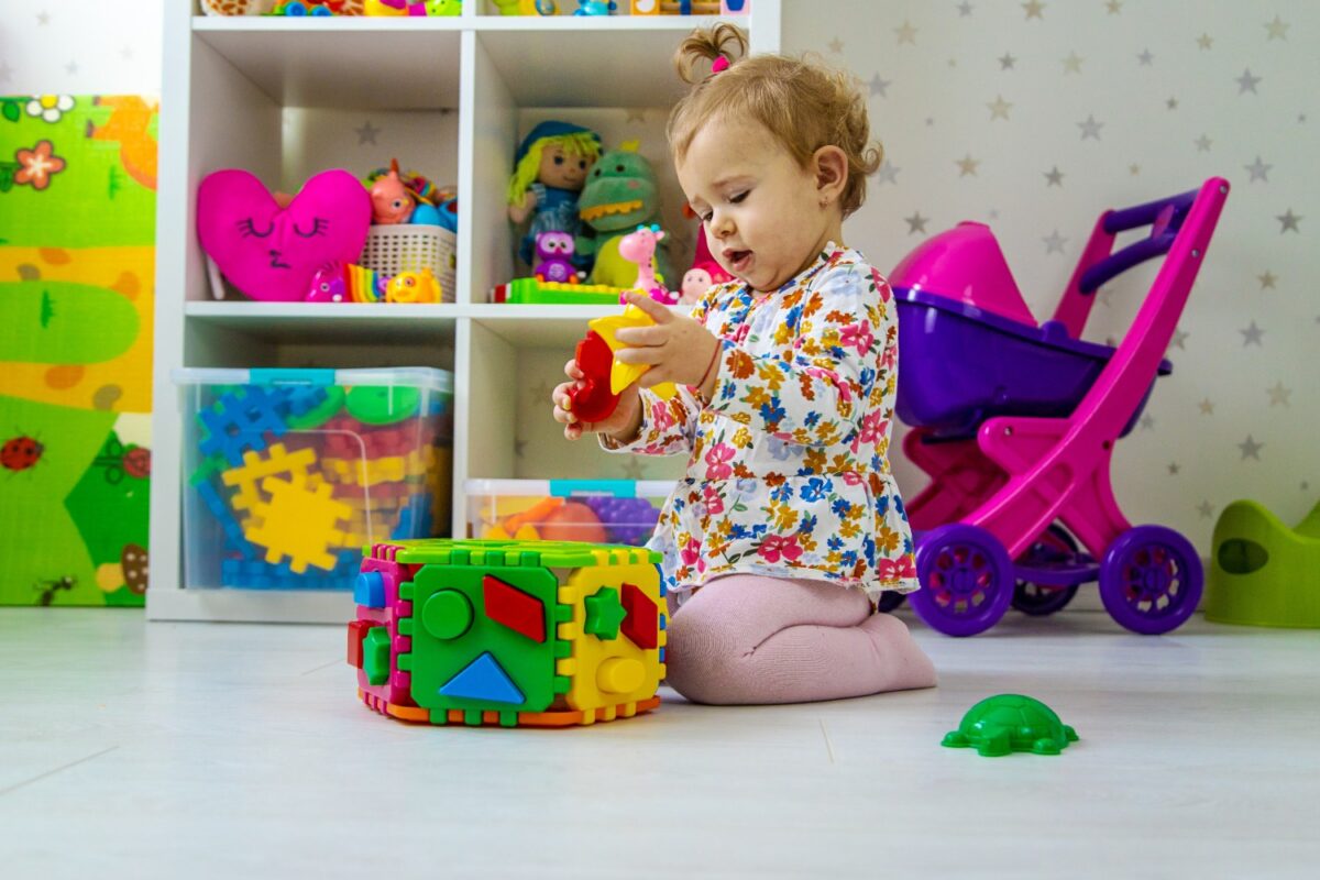 Toddler kneels on the floor, playing with bright, interlocking foam blocks in a colorful playroom.