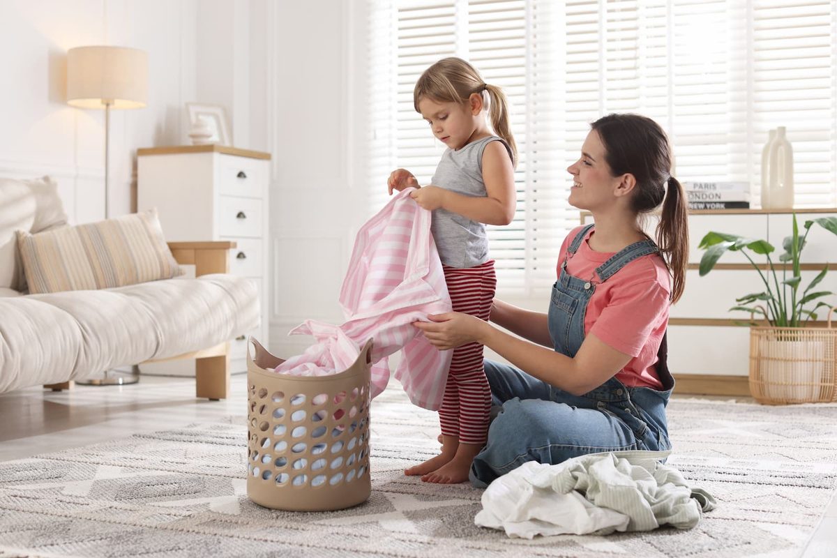 Mother and young daughter folding laundry together at home, demonstrating kindness and helpfulness through everyday chores.