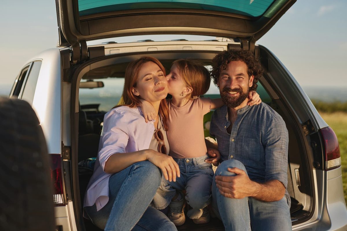 Happy family of three smiling and embracing in the open trunk of a car during a memorable family outing.