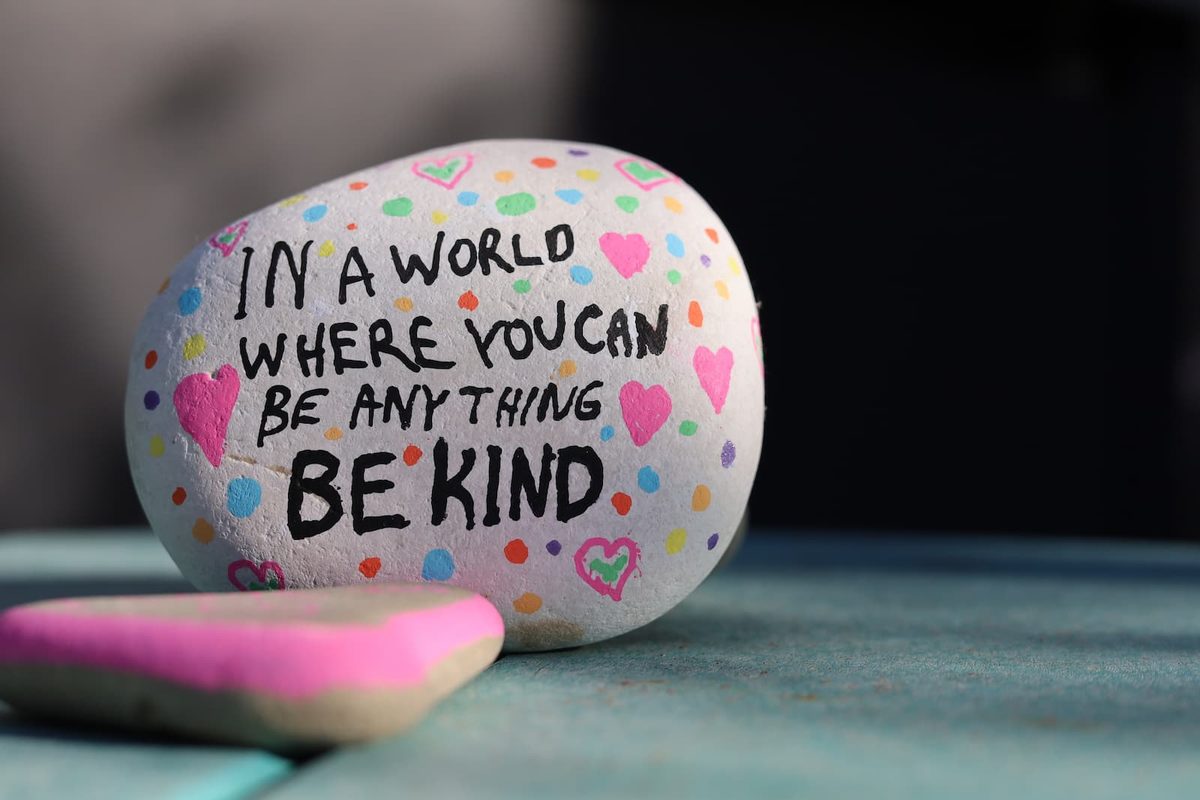Decorated kindness rock featuring the inspirational message “In a world where you can be anything, be kind,” surrounded by colorful hearts and dots.