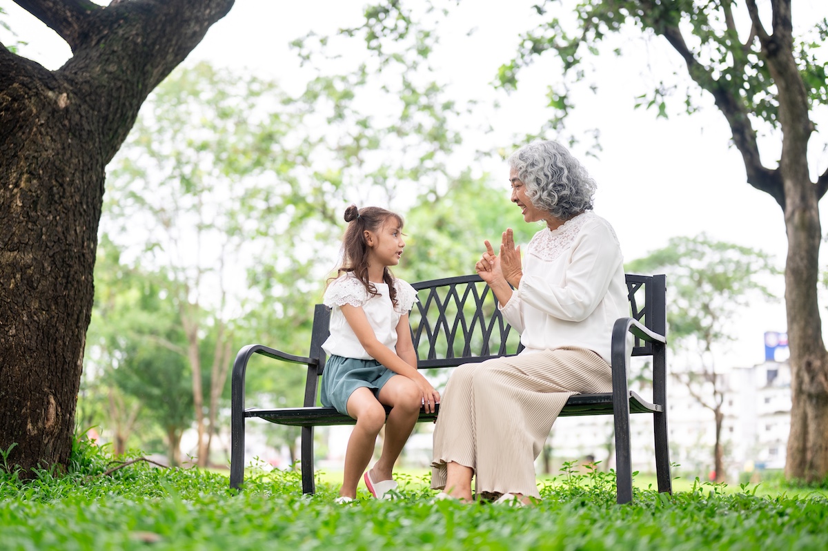 Young girl and her grandmother sitting together on a park bench, sharing a meaningful conversation outdoors.